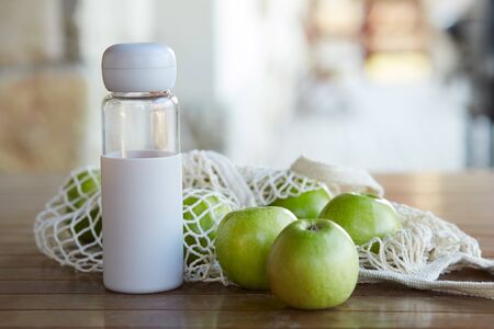 An eco bag with green apples and a bottle of water on a wooden tableの写真素材