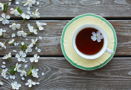 A cup of tea on a wooden background covered with cherry flowers.