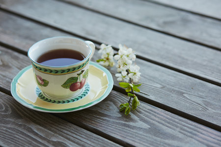 A cup of tea on a wooden background with a cherry branch