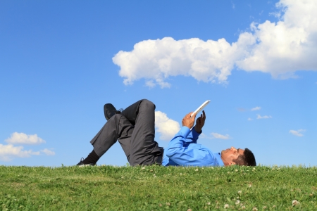 businessman laying down on the grass and working with tablet の写真素材