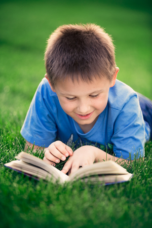 Boy reading book, lying down on green grassの写真素材