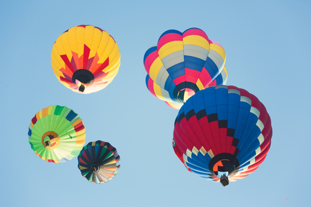 Multi colored hot air balloons flying up, group of balloons in sunny blue sky photographed from belowの写真素材