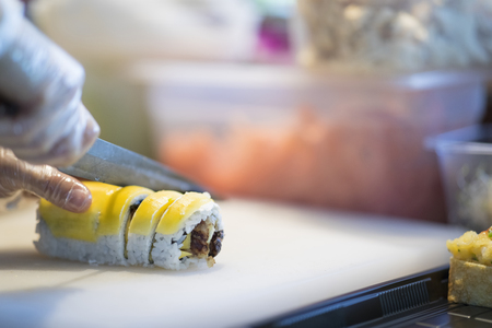 Sushi preparation in japanese restaurant, close up on chief hands cutting rollの写真素材