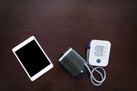 Digital blood pressure monitor with tablet on wooden tableの写真素材