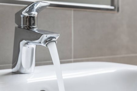 Bathroom faucet with running water into ceramic sinkの写真素材