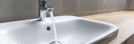 Bathroom faucet with running water into ceramic sinkの写真素材