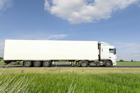 White transport truck driving on the road, green meadow with blue skyの写真素材
