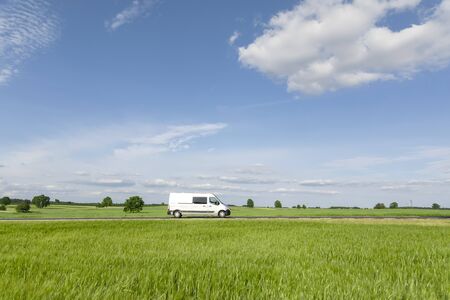 Transport van driving on the road, green meadow with blue skyの写真素材