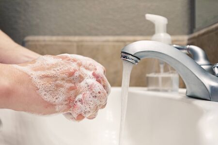 Washing hands with soap and water in bathroom sink, protection against covid-19 coronavirus flu virusesの写真素材