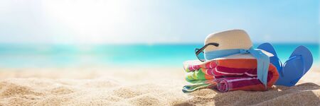 Beach accessories straw hat, flip flops, towel on sunny tropical beach, summer holidays vacation, Caribbean beach with turquoise water backgroundの写真素材