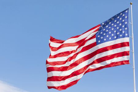 American flag waving in the wind on blue sky, US flag motion close-up, red white blue flag outdoors in sunlight. United States of America national flag. USA stars and stripesの写真素材