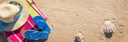 Beach towel with hat, sunglasses and flip flops photographed from above on sandy beachの写真素材