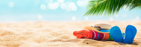 Summer holiday concept with flip flops and palm leaf on sandy beachの写真素材