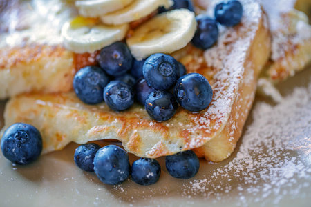 French toast with fresh blueberries and banana on white plate, close up
