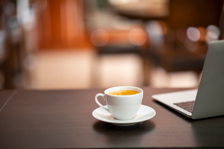 Coffee cup and laptop on wooden table in coffee shop.の写真素材
