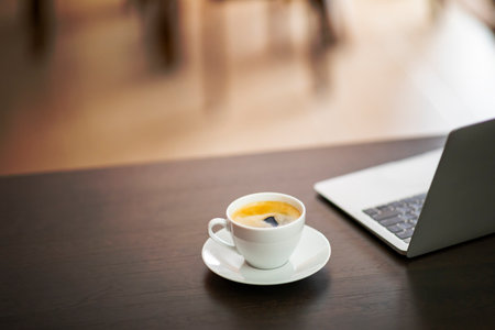 Coffee cup and laptop on wooden table in coffee shop.の写真素材