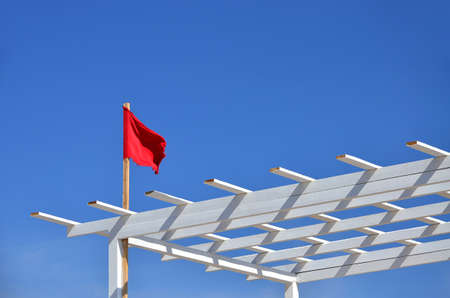 A red flag indicating a strong wind on the beach and the sea is flying in the wind on a white wooden...