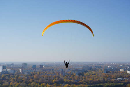 A paraglider flies a glider against the background of the city, houses and blue sky in good sunny weatherの写真素材