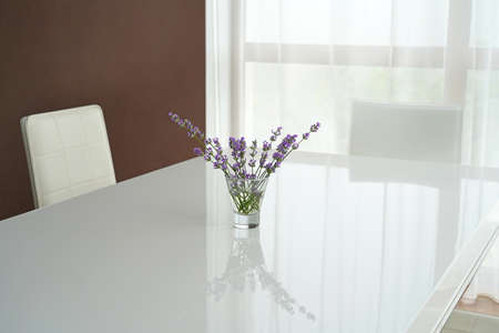 A white dining table with a bouquet of lavender and white chairs are in the living room in the house
