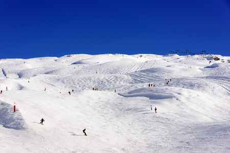 Wide area of ski slopes with a lot of rounded hills and skiiers spread out all over. White snow and clear blue sky only.の写真素材
