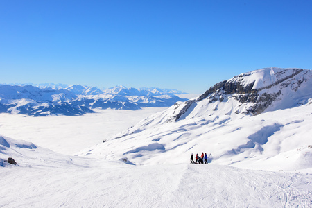 French and swiss alps above the clouds. A group of skiiers have stopped to take in the view. Snowy alpine mountain ridge in the background.の写真素材