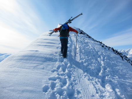One man walking in the snow on a mountain ridge towards the top. Lyngen Alps, Norway.の写真素材