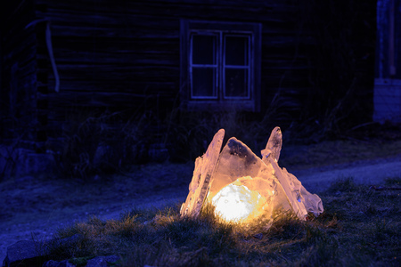 Natural ice forming a lantern lightned with a big candle. Outdoor night view with an old house in the background.の写真素材
