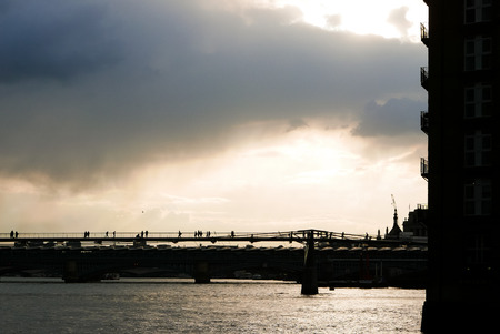 Silhuette of people walking on the London Millenium Bridge. Bright sunshine and cloudy sky.の写真素材