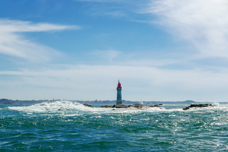 Lighthouse on a small rock outside Saint Malo. Waves and tidal current. Distant sailboat. Brittany, France.の写真素材