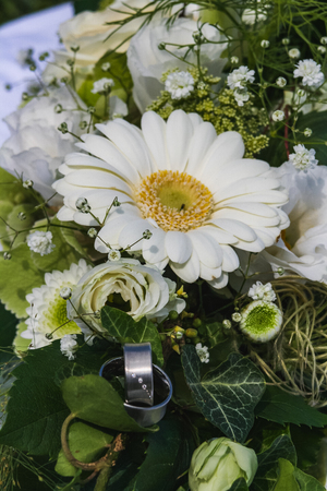 Two silver wedding rings with gems on creamy roses wedding bouquet close upの写真素材