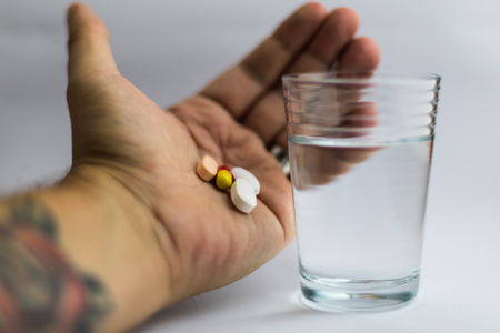 men showing pills in different colors beside a glass of water, medicineの写真素材
