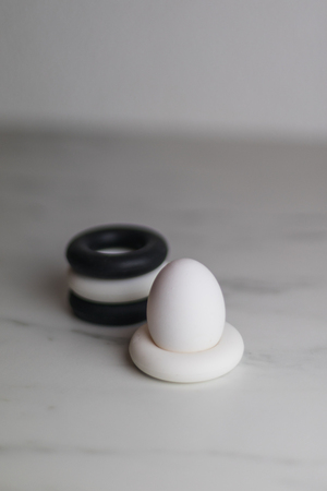 four black and white silicon eggcups on a marble table with only one egg, kitchenの写真素材