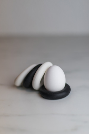 four black and white silicon eggcups on a marble table with only one egg, kitchenの写真素材