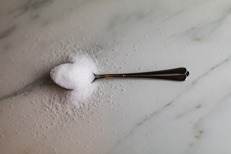 a silver metal spoon with too much salt in it on a marble table, kitchenの写真素材