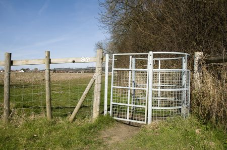 A metal farm gate with fields in the backgroundの写真素材