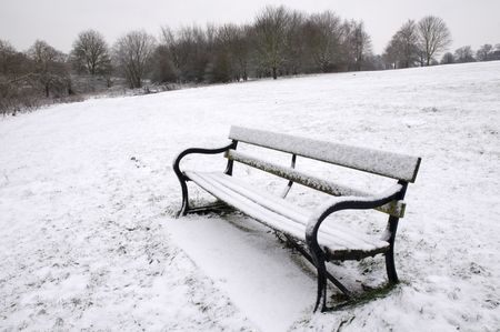 A path bench in a park covered in snow with trees in the backgroundの写真素材