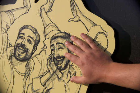 A hand touches a drawing of two smiling men.の写真素材