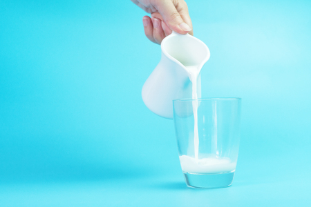 Milk poured into a glass on blue backgroundの写真素材