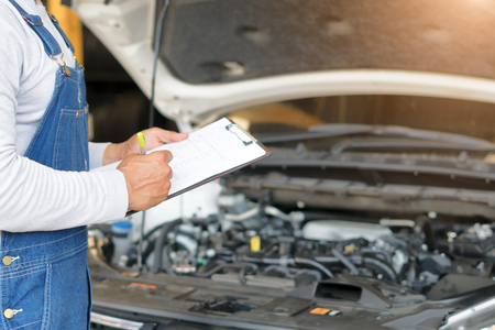 Mechanic engineer hand holding checklist paper and taking a note on clipboard with car engine background.の写真素材