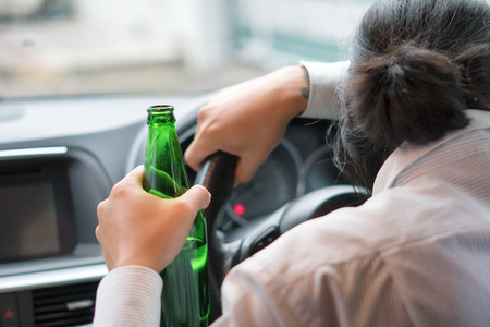 Drunk young man driving a car with a bottle of beer. Don't drink and drive concept. Driving under the influence. DUI, Driving while intoxicated. DWI.の写真素材
