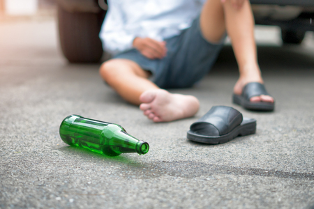 Drunken man sitting on the back of a car on the street.の写真素材