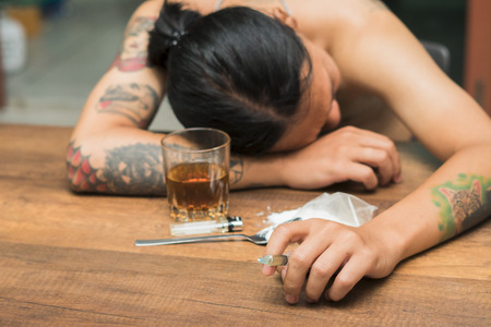 Male junkie hand trying to grab injection syringe of cooked heroine. Hard drug overdose and...