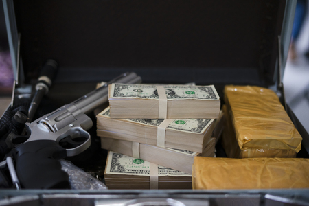 Drug trafficker holding a lot of cash on hand and use gun pushing drugs to the customer in the Drug dealing, concept about the drug problemの写真素材