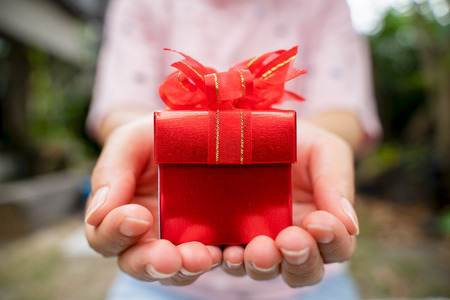 Red gift box in hand for giving in holidays. Give Valentine's Day gift box.