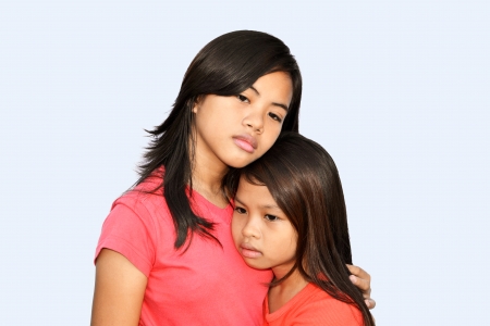 A teenager girl trying to comfort her younger sister with a hug & sad eyes!の写真素材