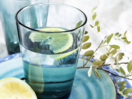 A glass of pure, fresh water with a slice of lemon on a turquoise plate, a good drink for hydrationの写真素材