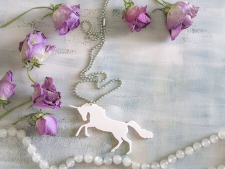 pale pink unicorn pendant with pink pearl string on a painted background with dry roses, copy spaceの写真素材