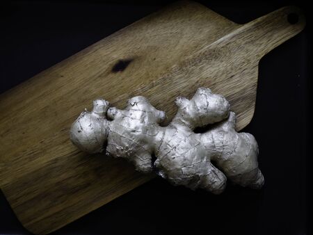 Ginger root on a brown wooden cutting board with black backgroundの写真素材