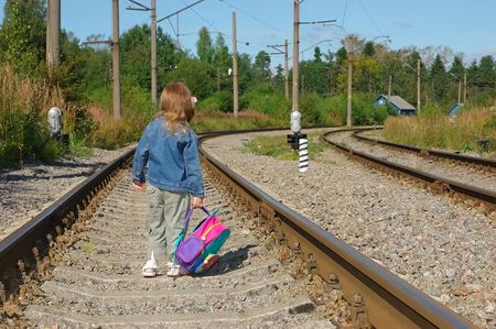 The little girl going with a backpack on railway railsの写真素材