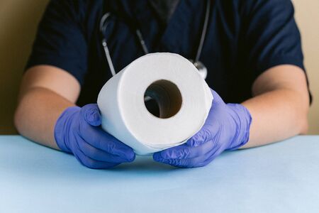 A medical professional with gloved hands holding a roll of toilet paper